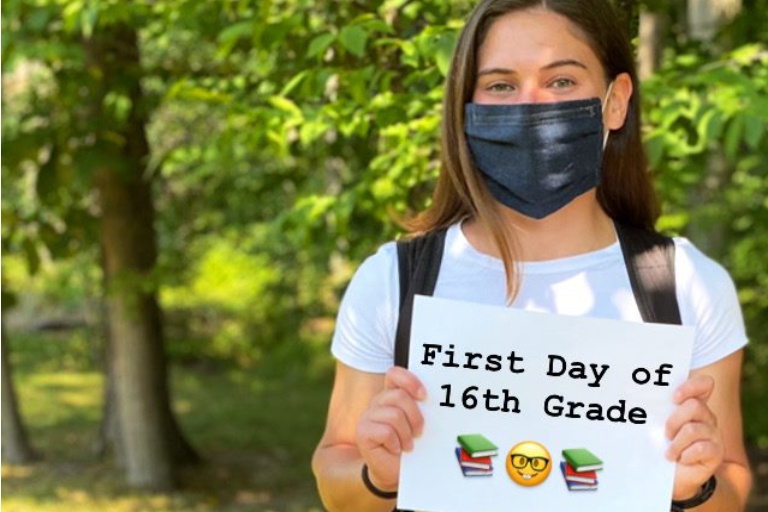 Senior Melanie Forbes, wearing a mask, holding a sign that says First Day of 16th Grade